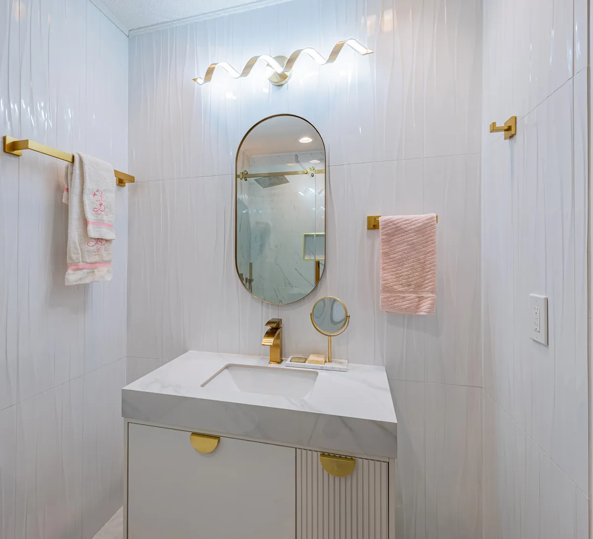 The fluted vanity and oval mirror, gold fittings against the ribbed tile