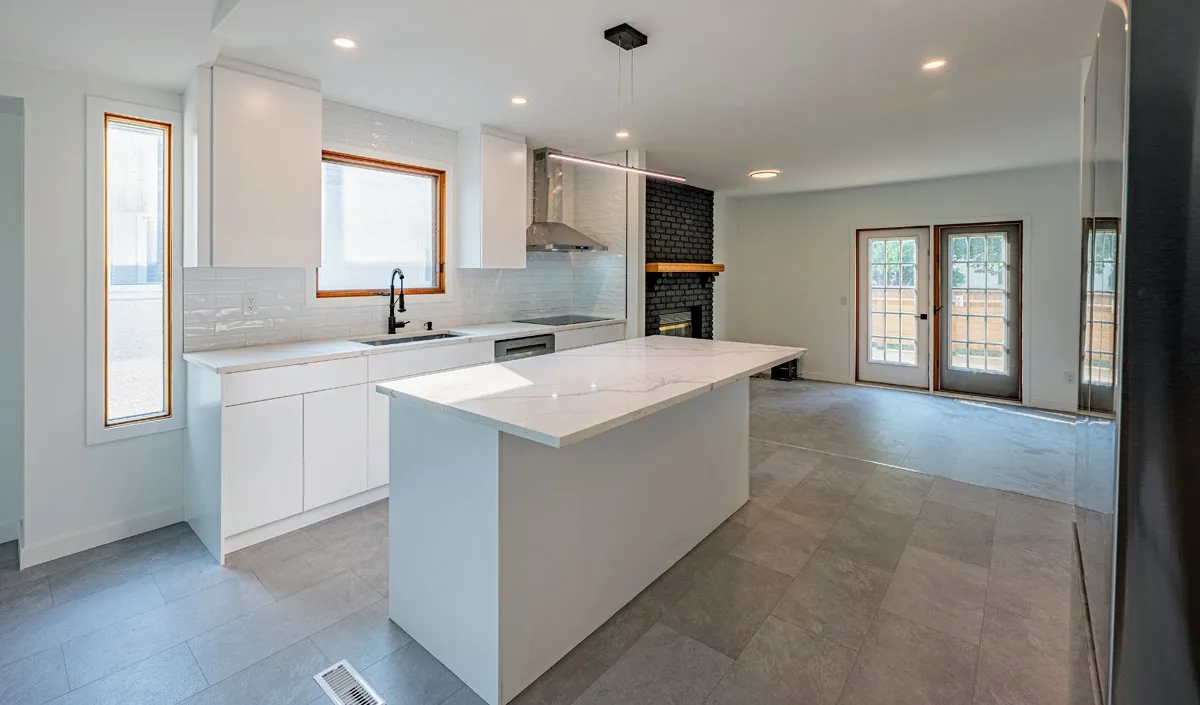 White kitchen with a quartz island, open through to the living end and the fireplace beyond