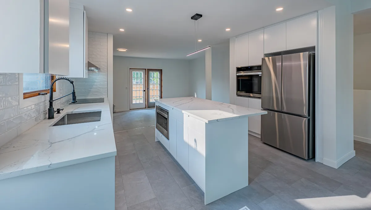 Kitchen island and sink run in veined quartz, wall oven and tall cabinetry alongside
