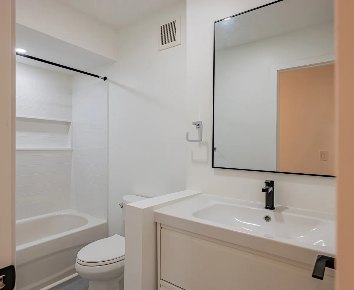 Renewed bathroom with a white vanity, black fittings and a tiled tub-shower