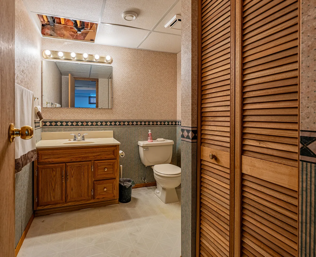 Before: the basement bathroom, an oak vanity and patterned wallpaper