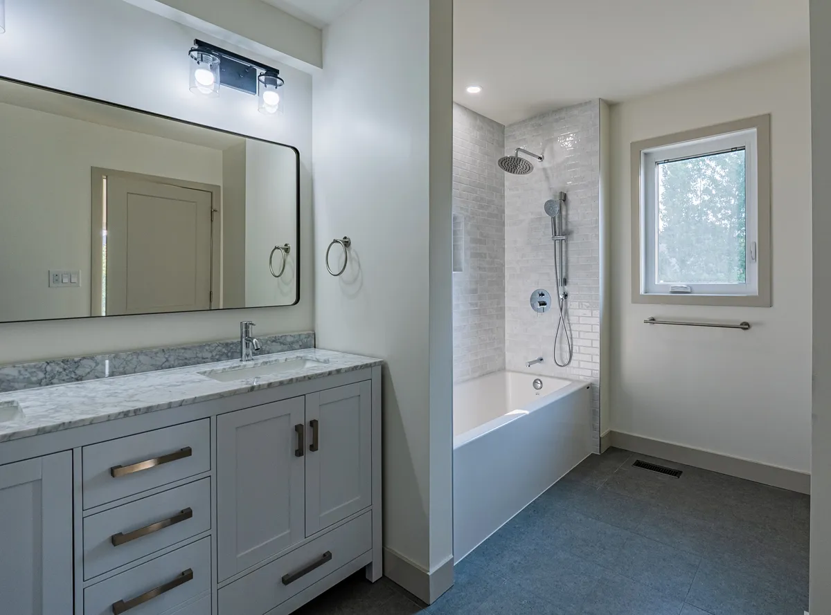 Bathroom with a grey double vanity, a wide mirror and a tiled tub-shower under the window