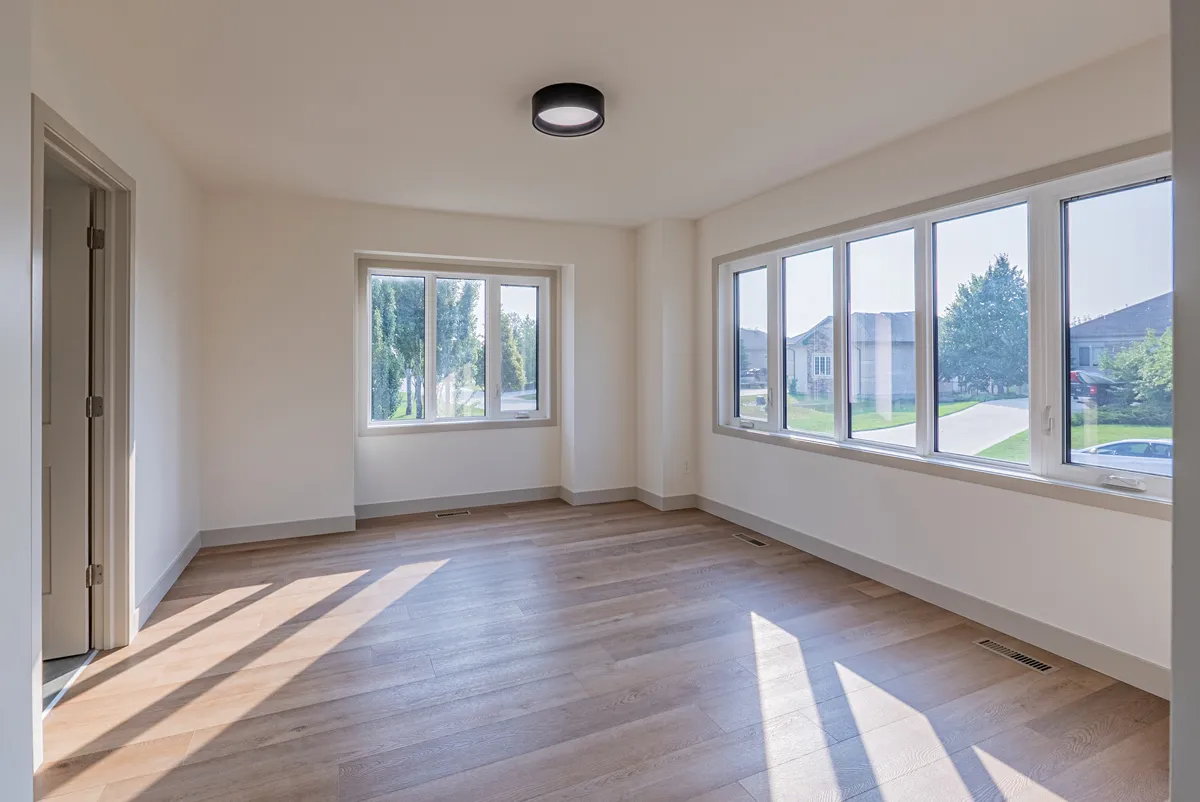 A bedroom with windows on two walls, sunlight across the plank floor