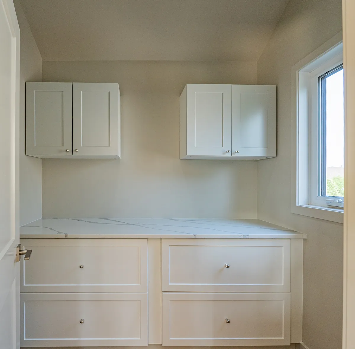 A built-in white counter over deep drawers, two small cabinets above it beside the window