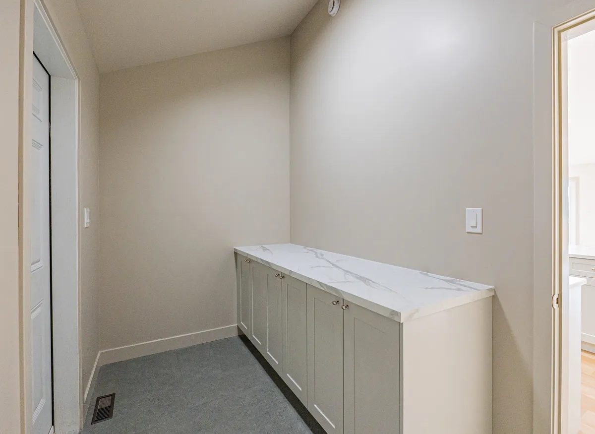 A long white counter over grey shaker cabinets along a side-room wall