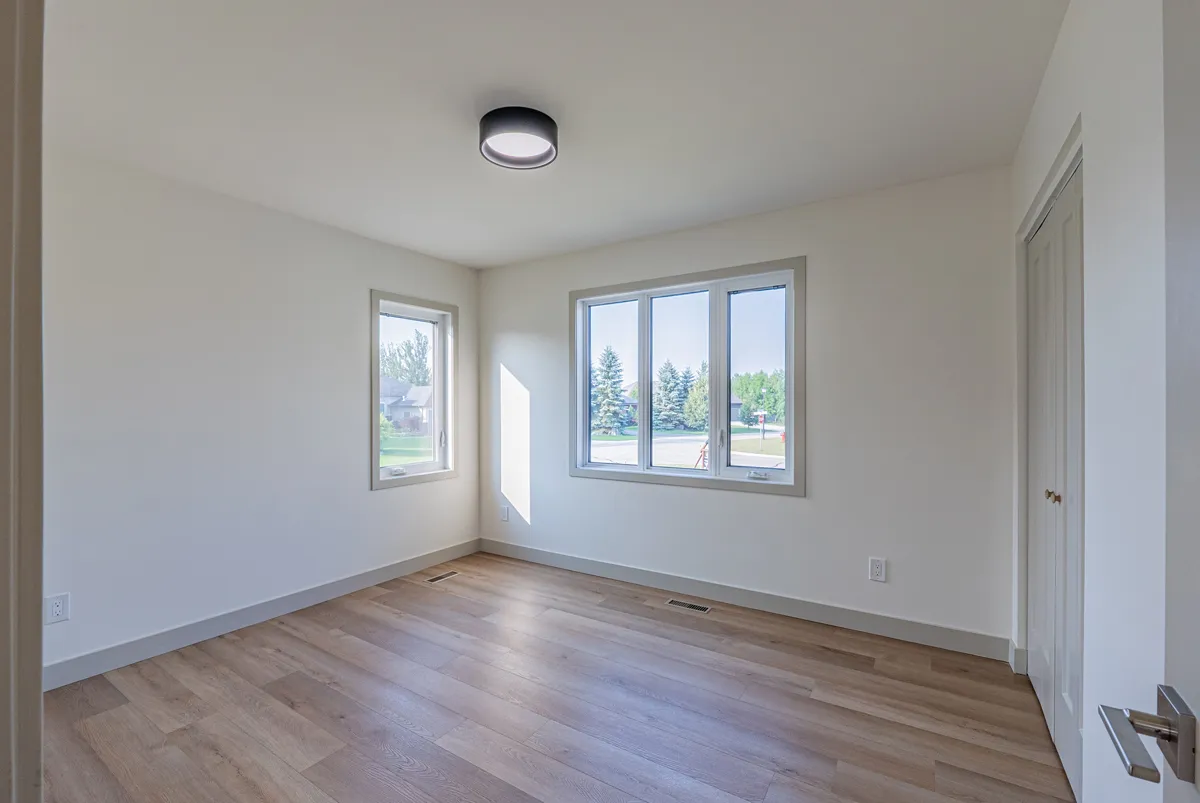 A bedroom with two windows, a little sun coming in across the floor