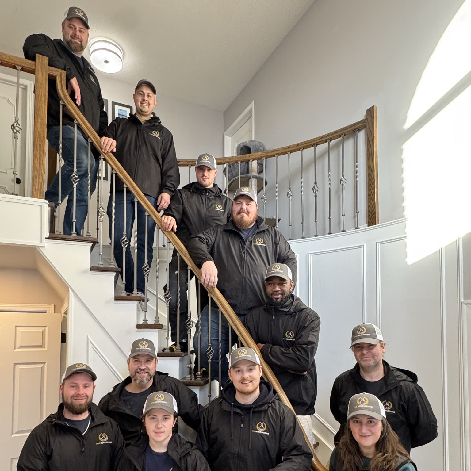The PHS Renovations crew in matching jackets and caps, posed up a curved staircase