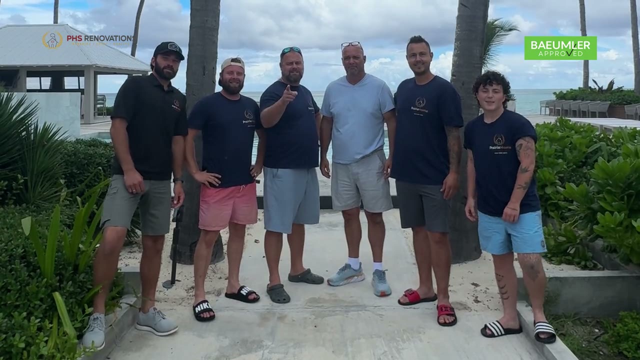 Six of the PHS Renovations team standing together outdoors, palm trees and the sea behind them